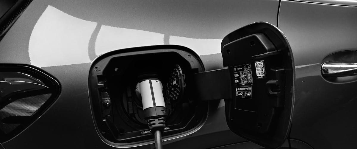 Close-up black and white image of an electric vehicle charging at a station.